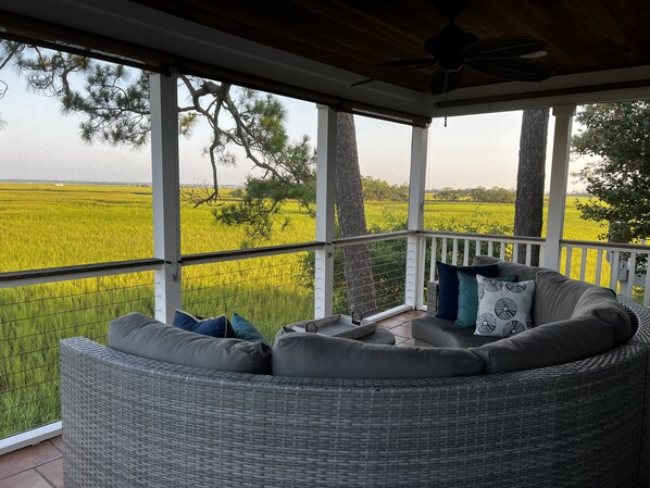 A covered porch with a wicker sofa and pillows, overlooking a green field. - Beautiful Marsh & Golf view. Walking distance to the beach & Conference Center. (Isle of Palms)