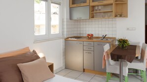 A compact kitchen with a dining area, a window, and a bed with pillows. - Room in Apartment - Cozy Studio Apartment for 2 (Baska Voda)