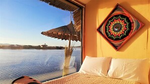 A bed with white pillows, a patterned wall hanging, and a view of water and buildings. - Room-suma Jakana Habitación Vista Al Ama (Puno)