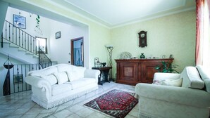 A living room with a white sofa, a patterned rug, a wooden cabinet, and a staircase. - Casa Vacanze Etna Cocus (Santa Venerina)