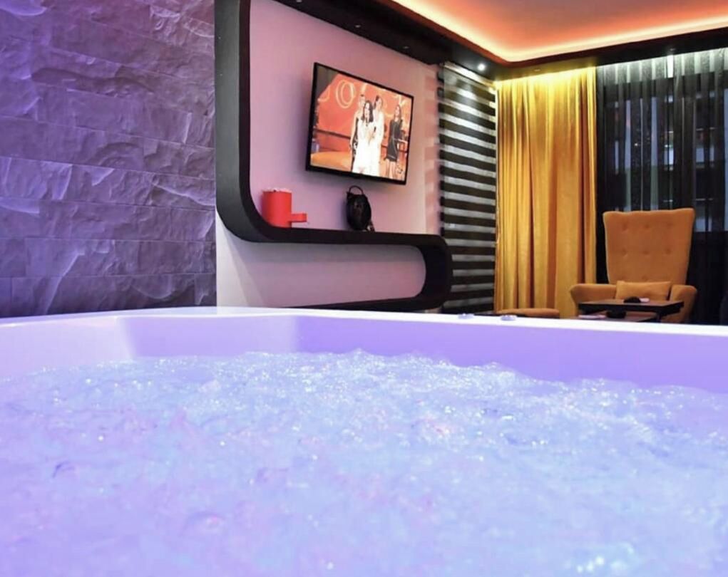 Una habitación con una bañera grande, un televisor montado en la pared y una silla.
