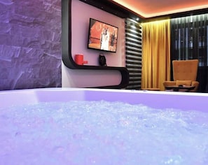 A room with a large bathtub, a television mounted on the wall, and a chair.