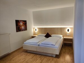 A bedroom with a wooden bed, two bedside tables with wall-mounted lights, a radiator, and a painting on the wall. - Residence Klementhof #4 (Naz Sciaves)