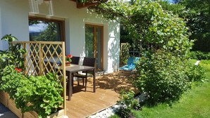 Eine Holzterrasse mit Tisch und Stühlen, ein überdachter Sitzbereich und ein Garten mit verschiedenen Pflanzen.