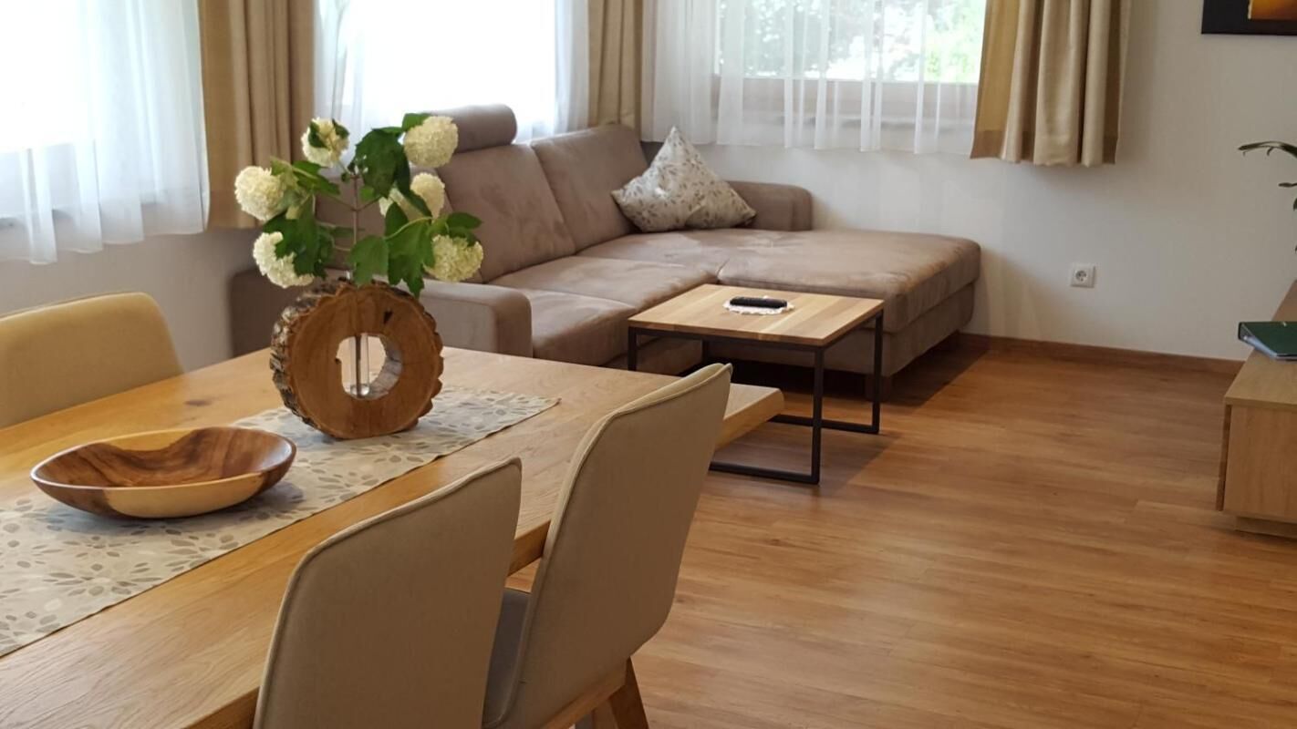 A living room with a sofa, a coffee table, a dining table with chairs, and a vase with flowers.