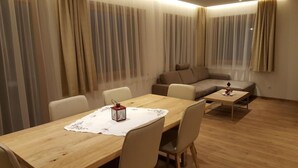 Ein gemütliches Wohnzimmer mit Esstisch aus Holz, beigen Sofas und einem kleinen Couchtisch.