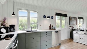 Una cocina moderna con paneles de madera blanca, una isla grande con cajones grises, un horno empotrado y una ventana con vista a zonas verdes.