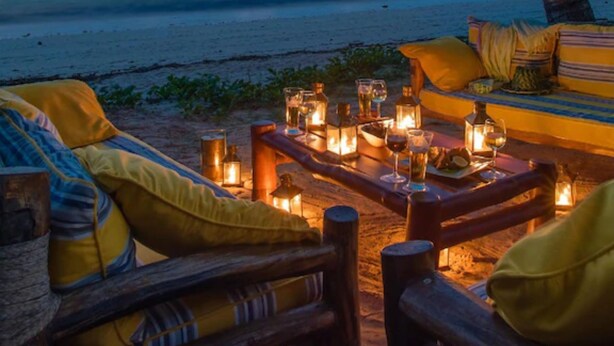 Eine Sitzgelegenheit am Strand mit Blick auf das Meer, ein Boot in der Ferne und eine Palme.