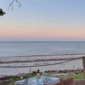 A table set for dining with a view of the sea, a lantern, and a rope barrier.