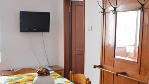 Ein Essbereich mit einem Tisch, der mit einer Sonnenblumen-Tischdecke bedeckt ist, einer Vase mit Früchten und einem an der Wand befestigten Fernseher.