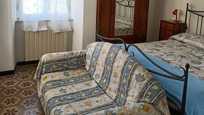Ein Schlafzimmer mit einem Bett, einer Couch, einem Holzschrank und einem Fenster mit Spitzenvorhängen.