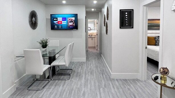 A modern hotel room with a dining area, a TV mounted on the wall, and a hallway leading to a bathroom. - 💎💎stylish 2 Bedrooms Apartment By Miami Airport (Miami)