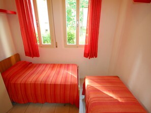 Une chambre avec deux lits, chacun recouvert d’une couvre-lit à rayures, deux fenêtres avec des rideaux et une tête de lit en bois.
