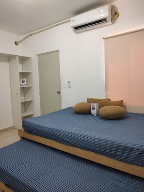 Un dormitorio con una cama litera, un aire acondicionado blanco, una puerta y un estante con una caja.