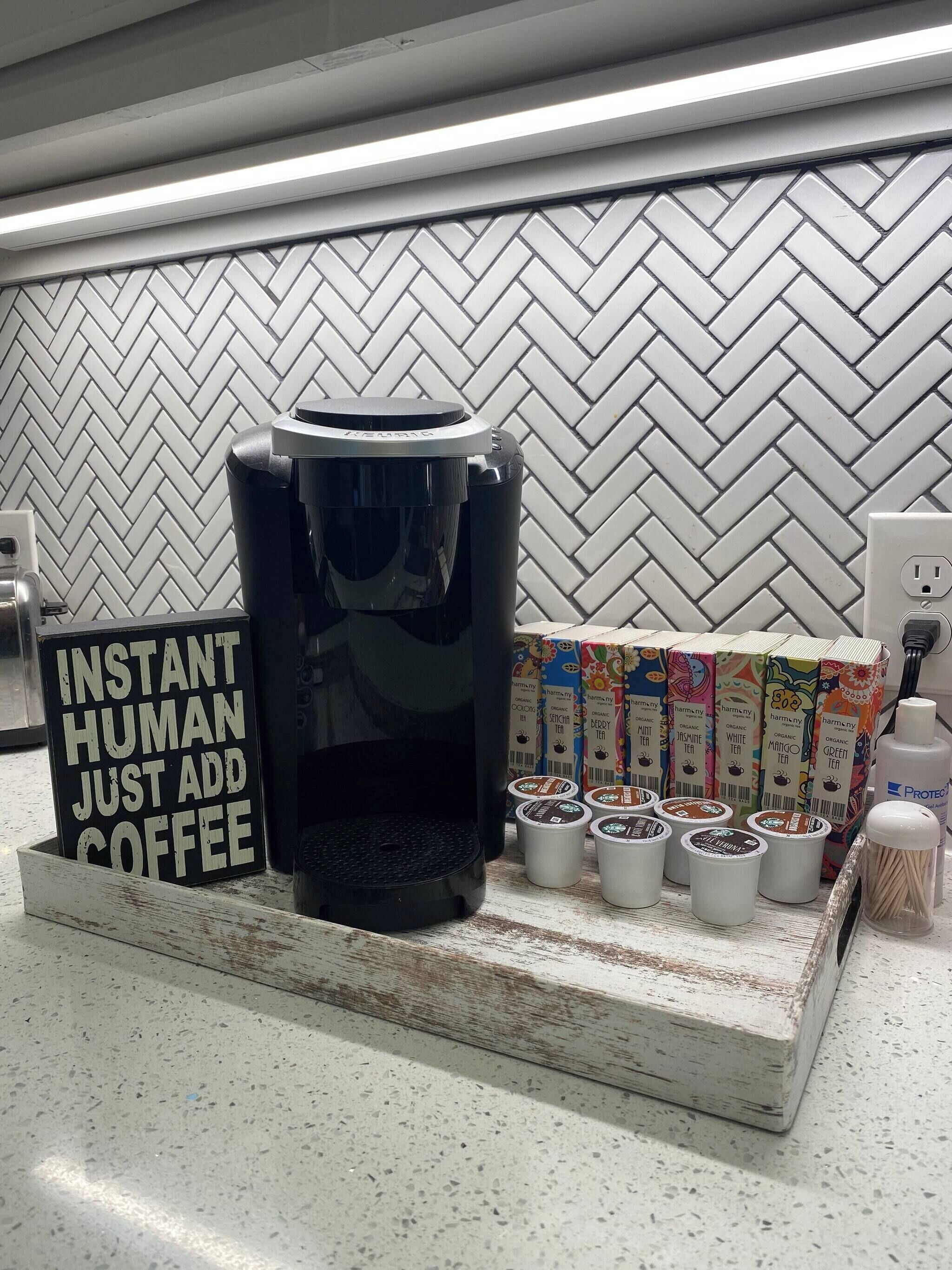 Une machine à café, des sachets de café instantané et une pancarte sur laquelle on peut lire : « CAFÉ INSTANTANÉ, AJOUTEZ SIMPLEMENT DU CAFÉ » – le tout dans un décor de cuisine.