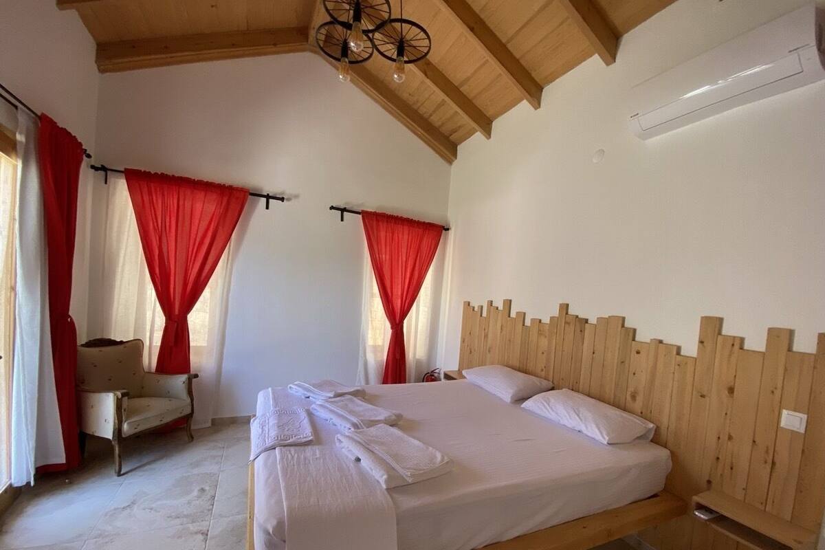 A bedroom with a wooden headboard, a bed with white linens, red curtains, and a chair.