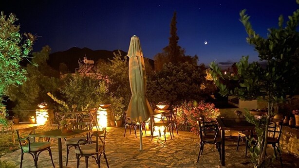 Un patio al aire libre con piso de piedra, varias mesas y sillas, y una sombrilla central.