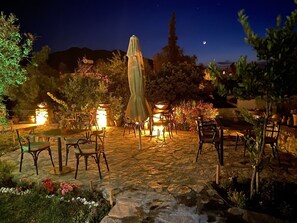 Un patio al aire libre con piso de piedra, varias mesas y sillas, y una sombrilla central.