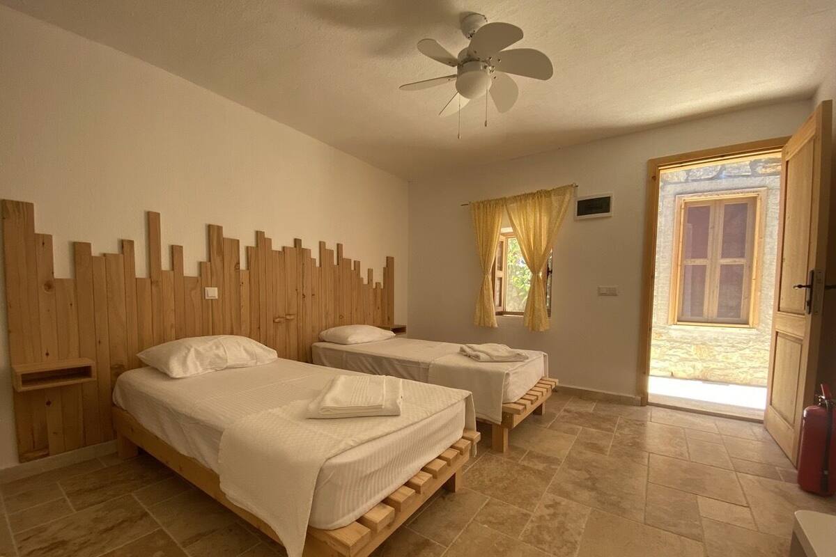 A room with two wooden beds, a ceiling fan, and a window with curtains.