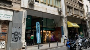 A multi-story building with a storefront featuring a green awning and a sign for a shop. - Starla Studios (Athens)