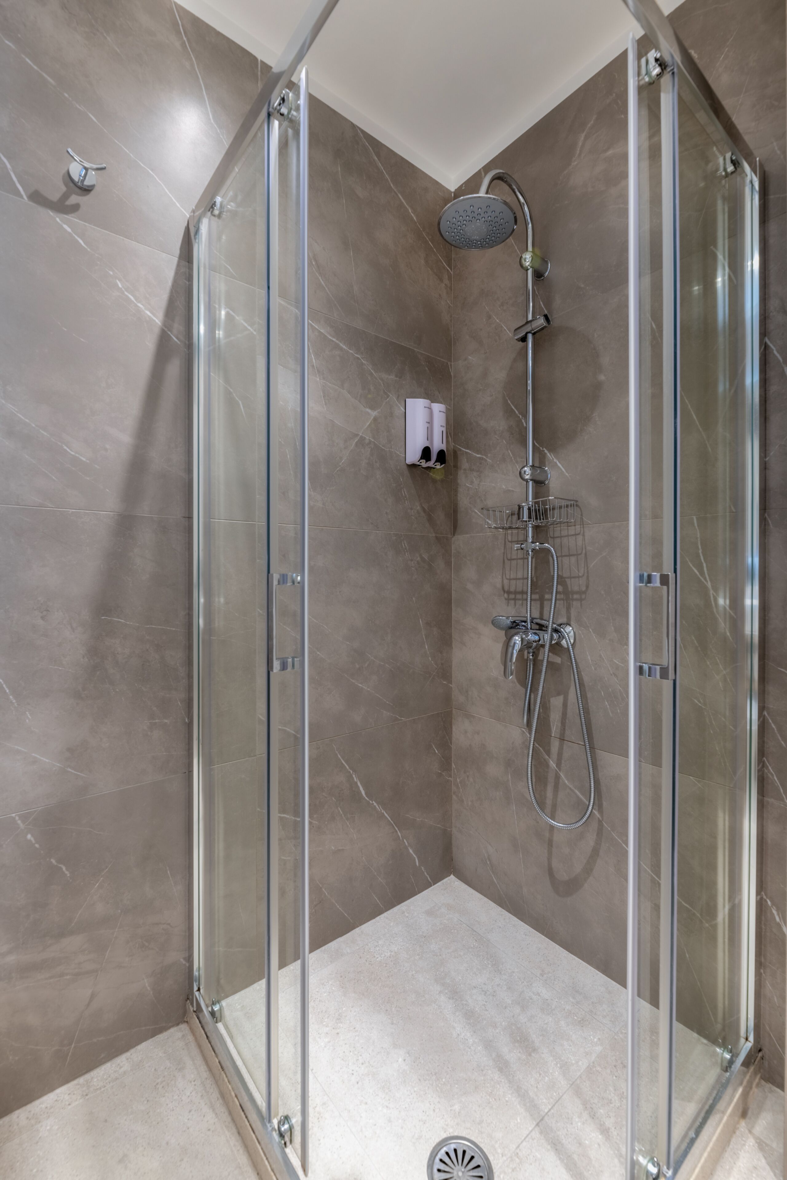 A glass-enclosed shower stall with a handheld showerhead and a wall-mounted faucet.