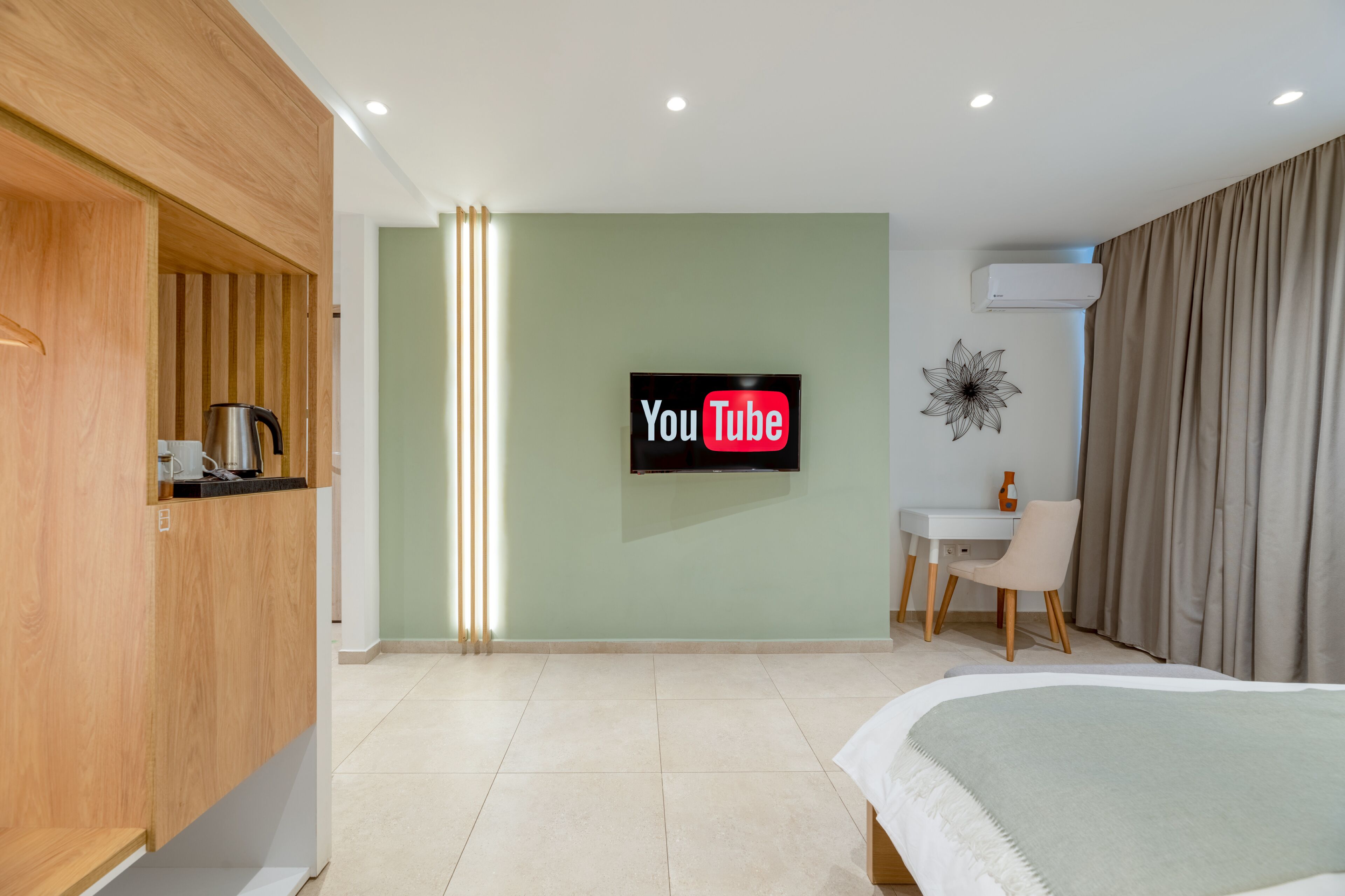Una habitación de hotel moderna con una cama, un escritorio, una silla, un televisor montado en la pared y un equipo de aire acondicionado.