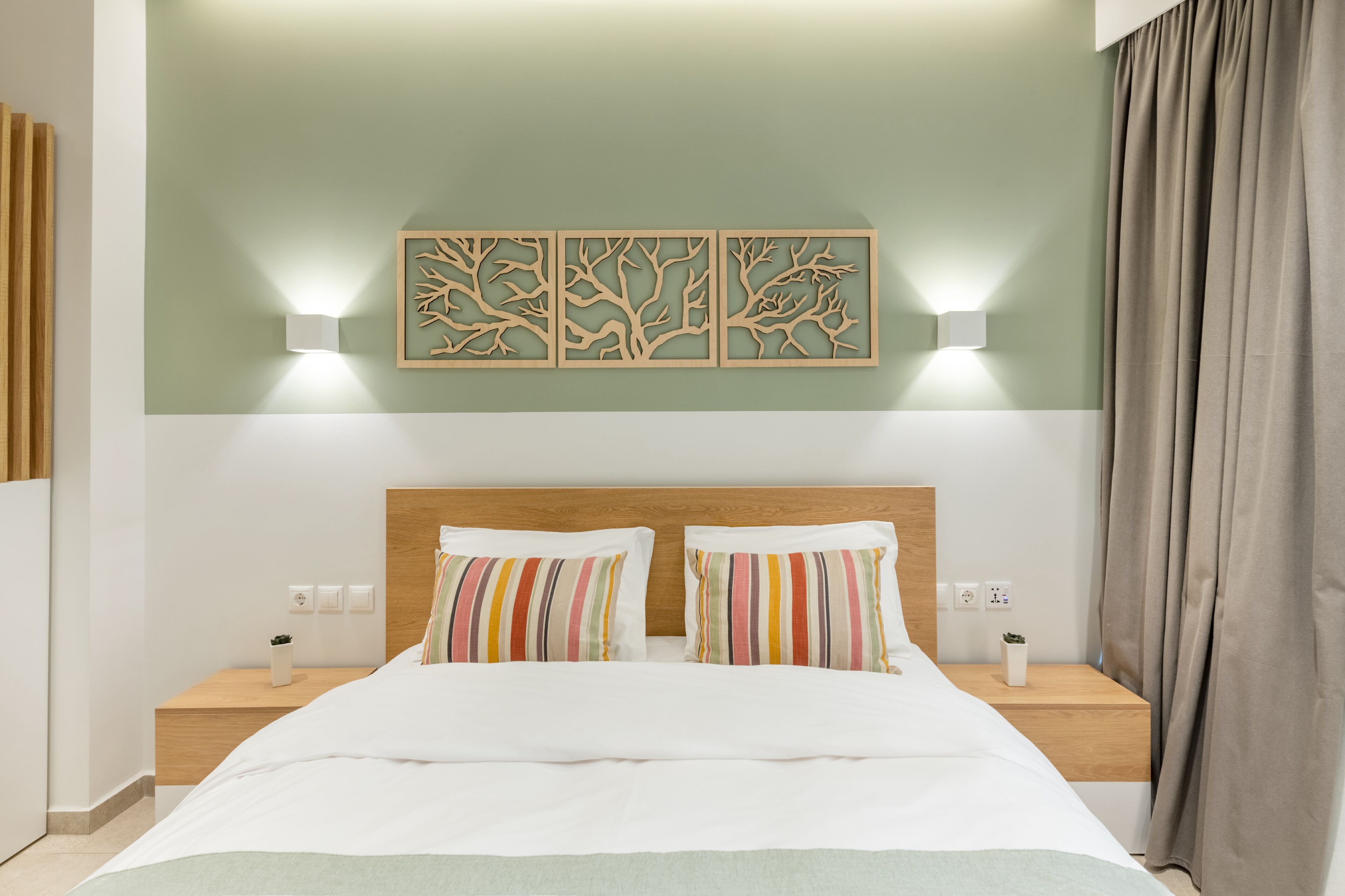 A neatly made bed with striped pillows, a wooden headboard, and two bedside tables with wall-mounted lamps.