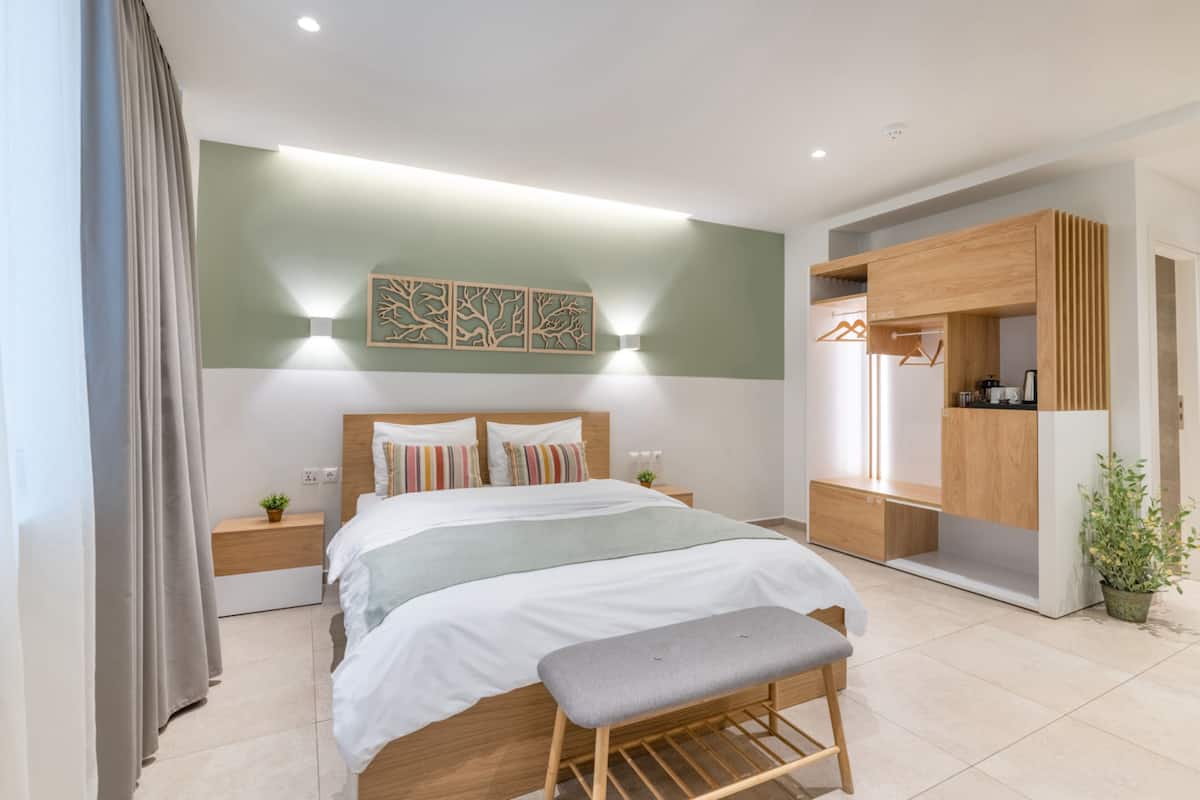 A modern bedroom with a bed, bedside tables, a bench, a wardrobe, and a wall-mounted light fixture.