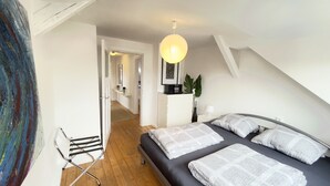 Quarto com cama, mesa de cabeceira, luminária e vista para o corredor.