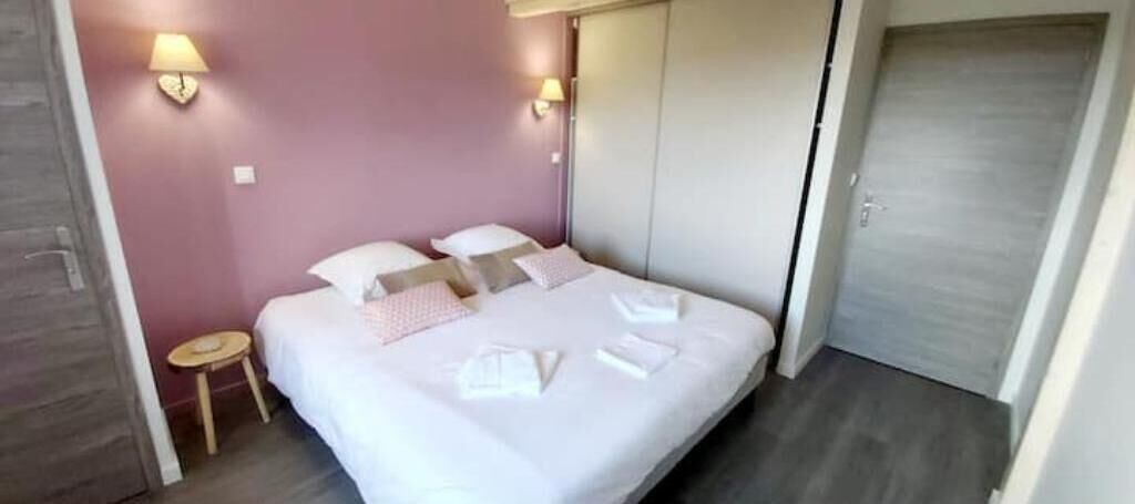 Een opgemaakt bed met kussens en handdoeken, een nachtkastje en een garderobe in een kamer met een roze muur en een deur.