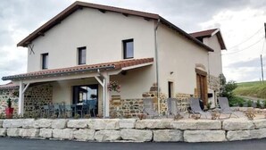 Una casa de dos pisos con fachada de piedra, un patio cubierto y un muro de piedra que rodea la propiedad.