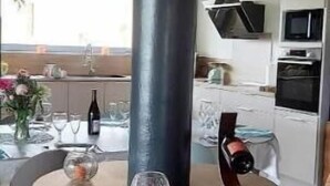 Un interior rústico con un estufa de barril de madera, una mesa de comedor dispuesta con vasos y una botella, y una zona de cocina con electrodomésticos.