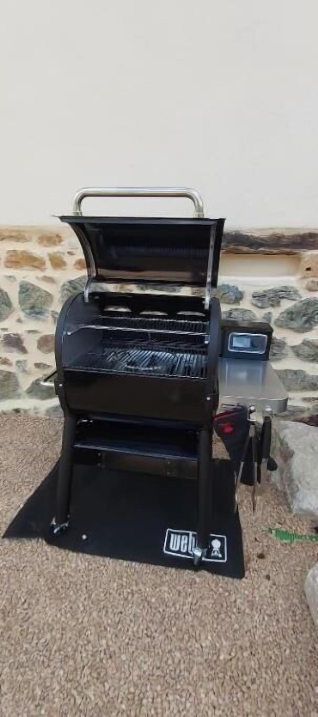 A black barbecue grill with a clear lid, placed on a carpeted surface outdoors.