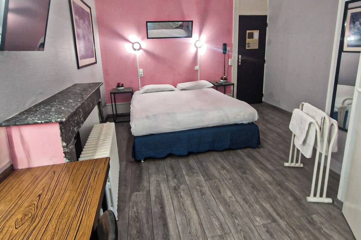 A hotel room with a bed, bedside tables, a desk, and a mirror.