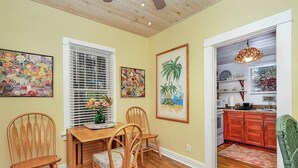 Un comedor con una mesa y sillas de madera, una ventana con persianas, y dos cuadros en la pared.