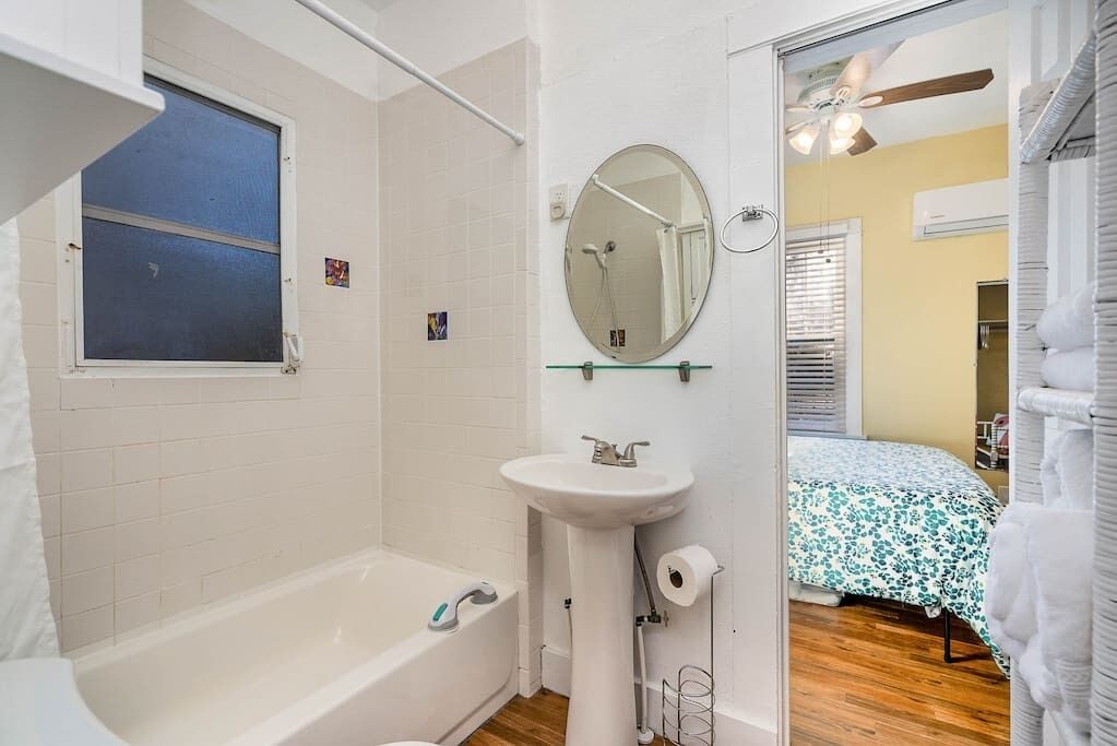 A bathroom with a bathtub, a sink, a mirror, and a window.