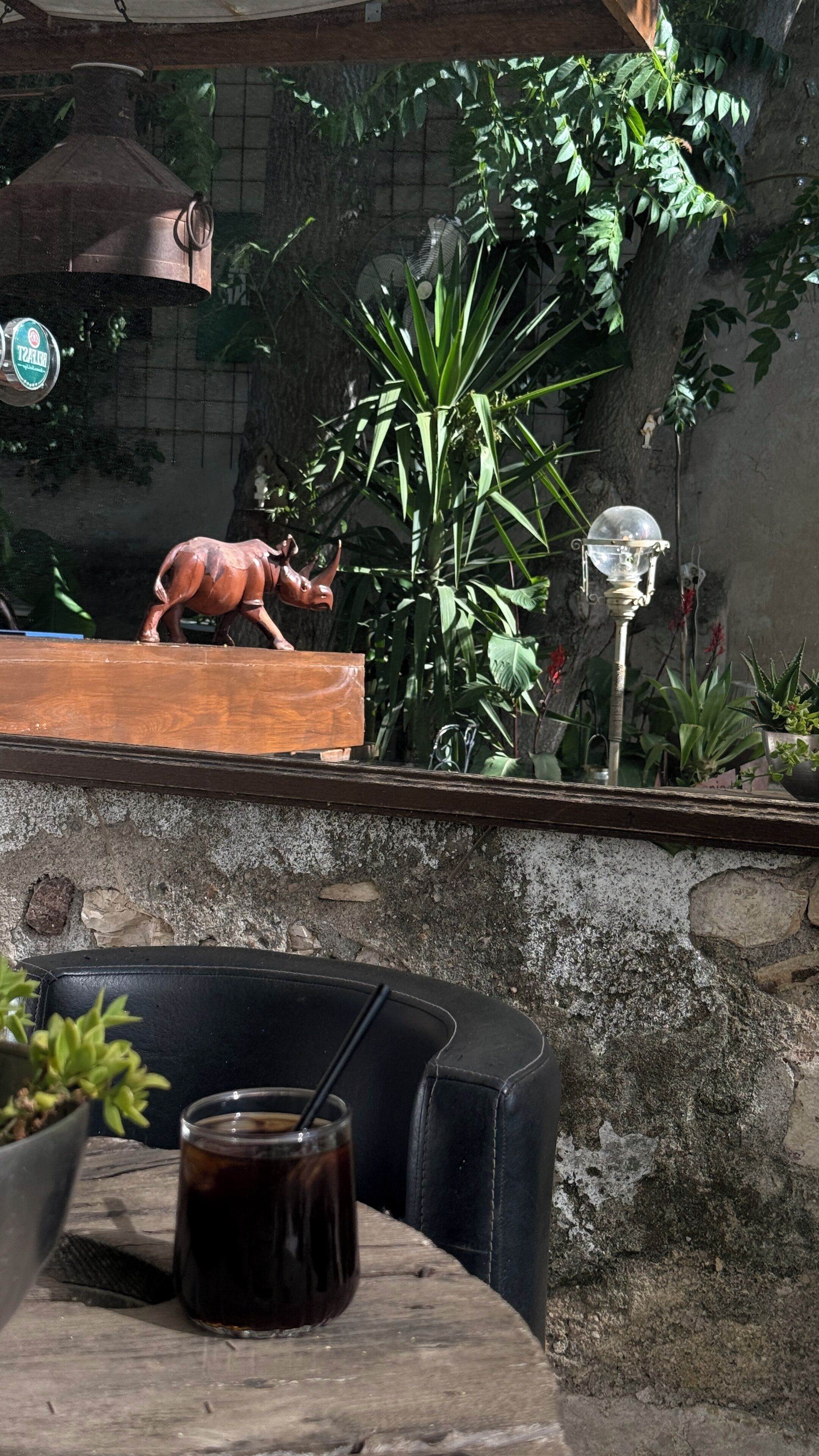 A rustic outdoor seating area with a wooden table, a glass of dark beverage, and a decorative animal figure.