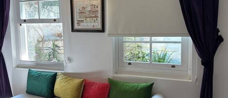 A room with a white sofa, two windows with curtains, a wall-mounted lamp, and a framed picture.