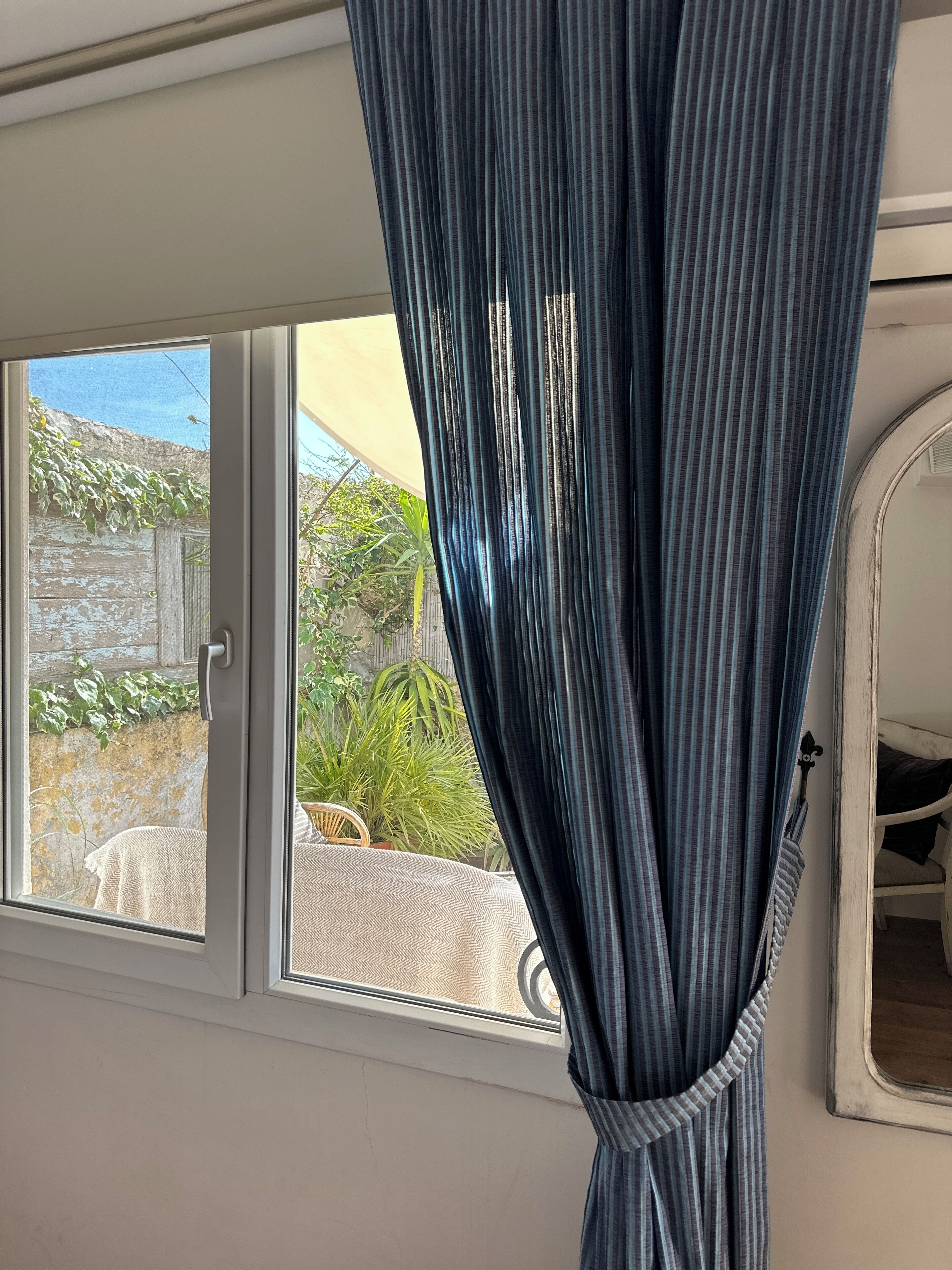 A room with a window, a curtain, a bed, and a mirror.