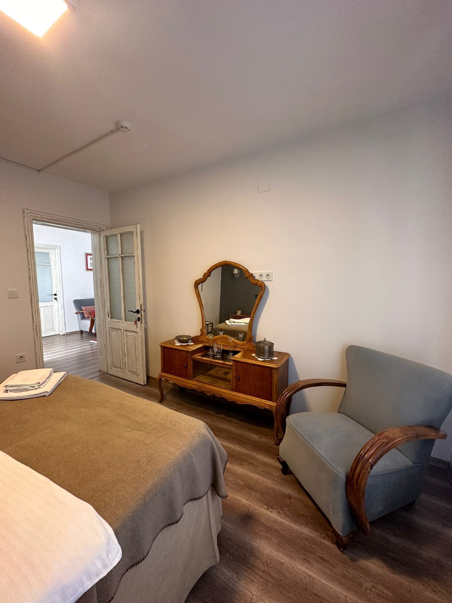A bedroom with a bed, a chair, a dresser with a mirror, and a door leading to another room.