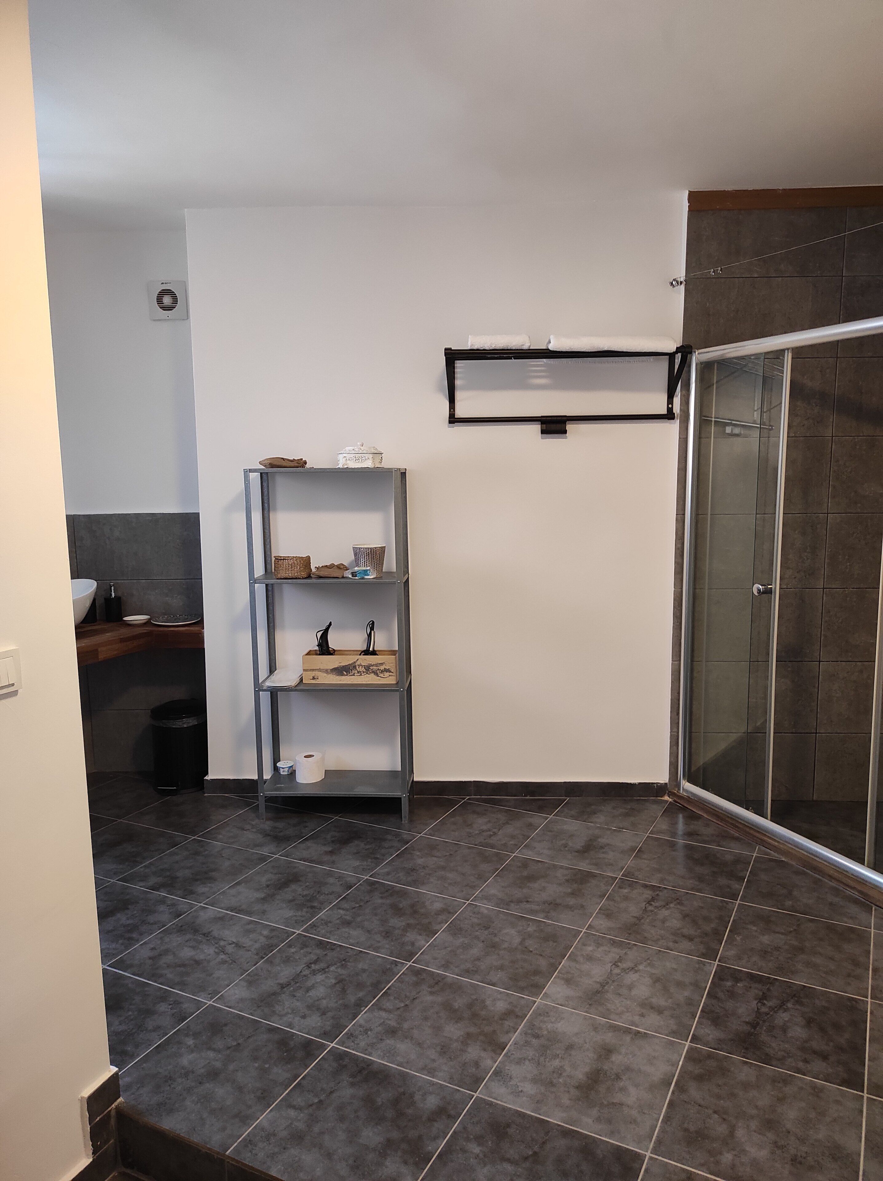 Un baño con ducha, un estante con artículos de aseo y un perchero para toallas.