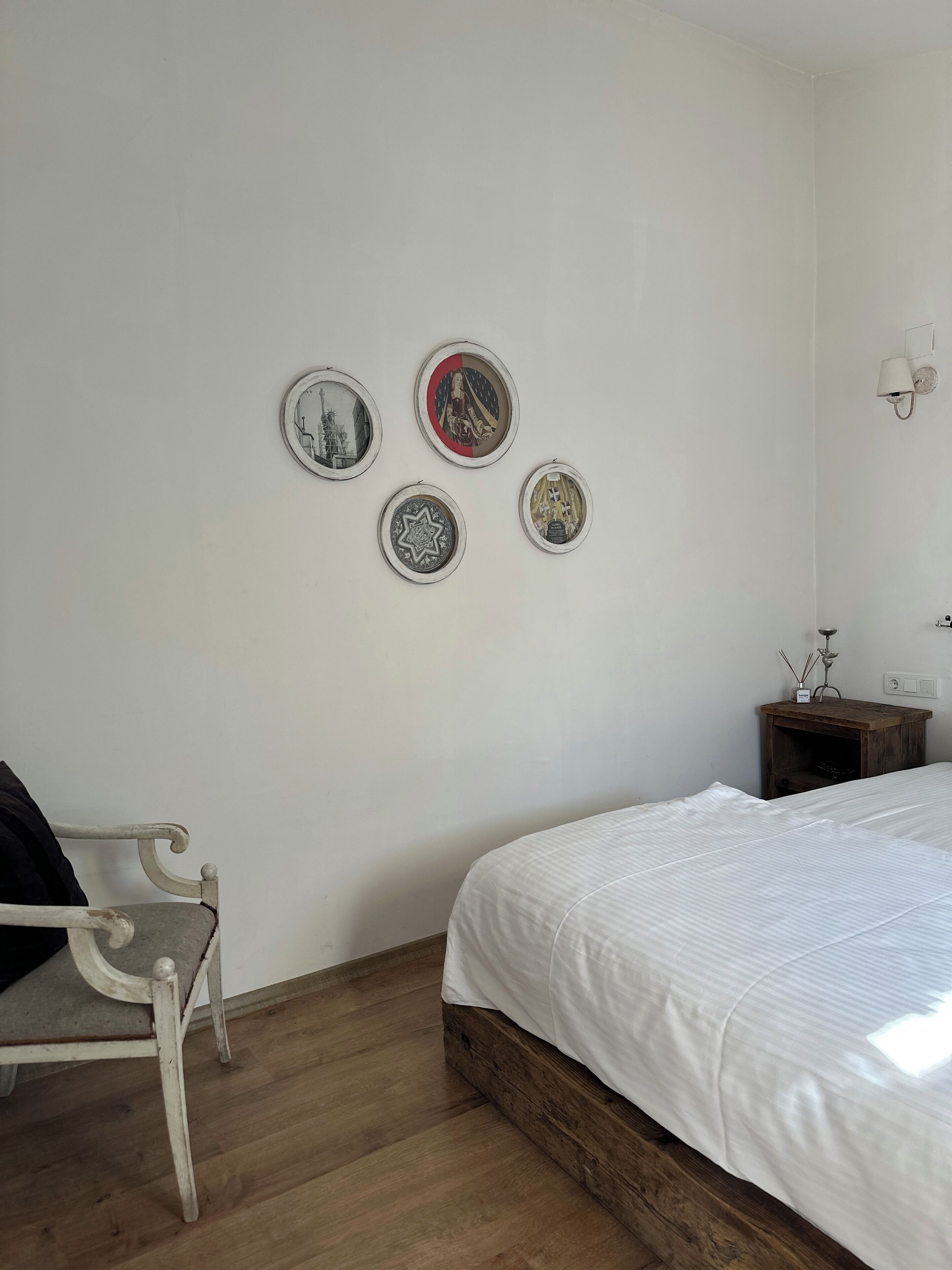 A bedroom with a wooden floor, a white bed, a white chair, and four framed pictures on the wall.