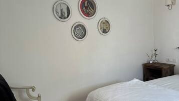 A bedroom with a wooden floor, a white bed, a white chair, and four framed pictures on the wall.
