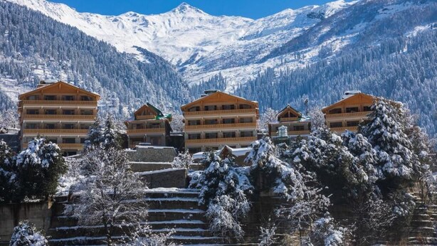 Un hôtel composé de plusieurs bâtiments en bois, situé dans un cadre magnifique, avec en toile de fond des montagnes et des arbres couverts de neige.