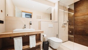 A modern bathroom with a wooden vanity, a toilet, and a glass shower enclosure. - Hotel VIVO (Schierling)