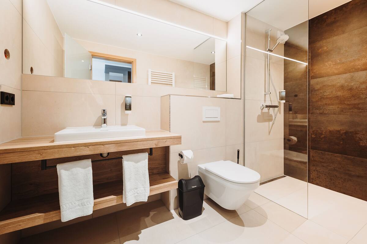 A modern bathroom with a wooden vanity, a toilet, and a glass shower enclosure.