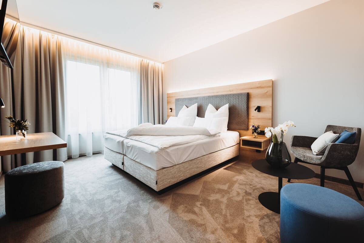 A modern hotel room with a large bed, a desk, a chair, and a small table.
