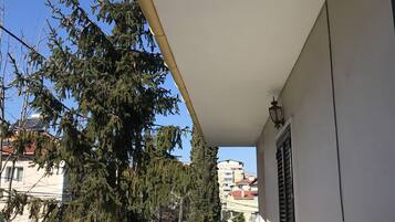 A balcony with a tiled floor, a white wall, and a window with shutters.