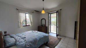 Une chambre à coucher comprenant un lit, une commode, un miroir, une fenêtre avec des rideaux et une porte donnant sur un balcon.