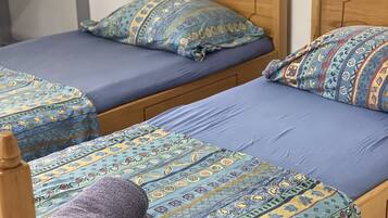 Two wooden beds with blue bedding and patterned pillows, a small table, and a plain wall.